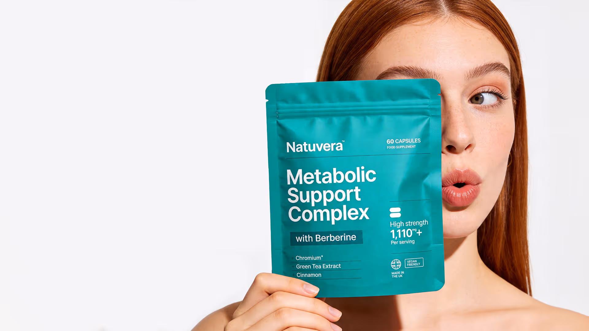 Red-haired woman holding Natuvera Metabolic Support Complex supplement pouch covering part of her face.