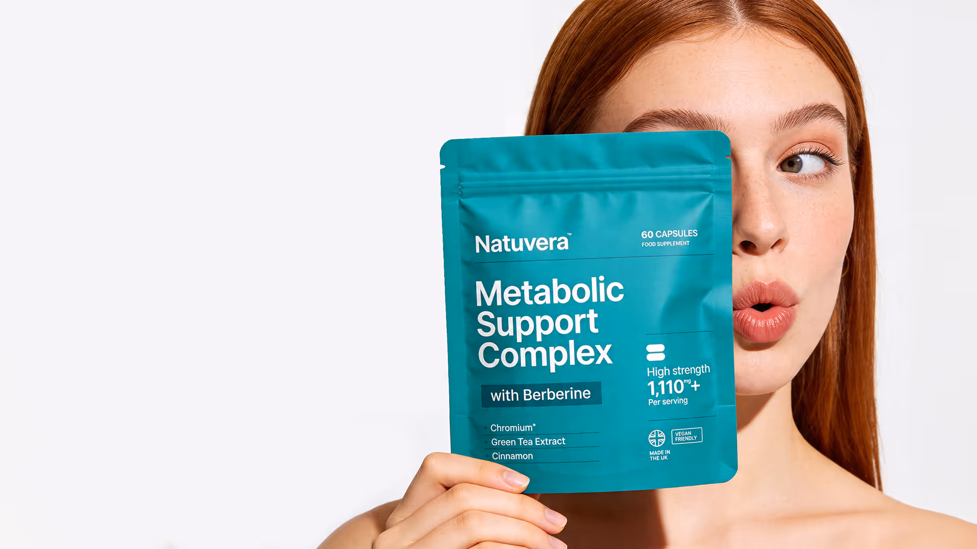 Red-haired woman holding Natuvera Metabolic Support Complex supplement pouch near her face.